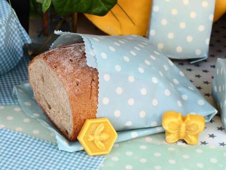 Ein halbes Brot in blau-weiß gepunktetem Bienenwachstuch, daneben gelbe Wachsfiguren in Schmetterlings- und Bienenform.