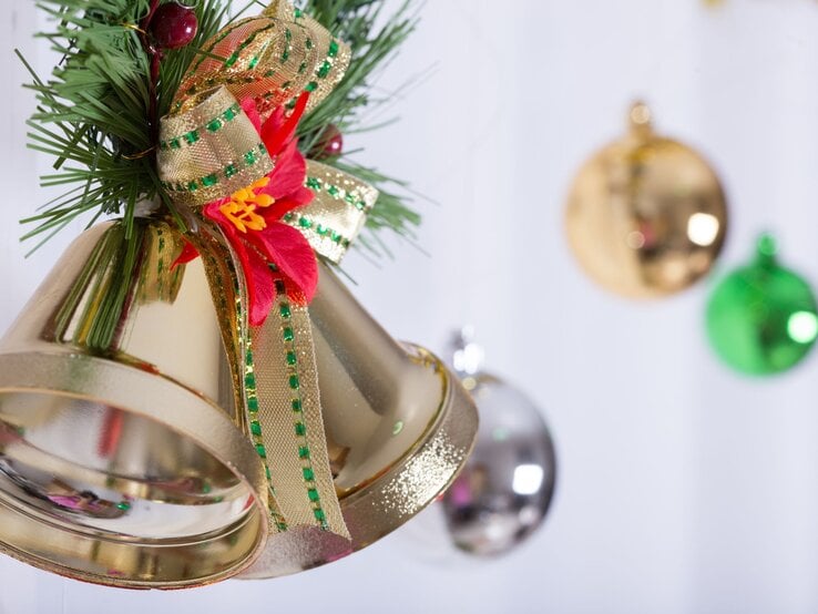 Nahaufnahme von goldenen Weihnachtsglocken aus Blumentöpfen mit Schleife und Blüte, im Hintergrund schimmernde Christbaumkugeln in Weiß, Grün und Gold.