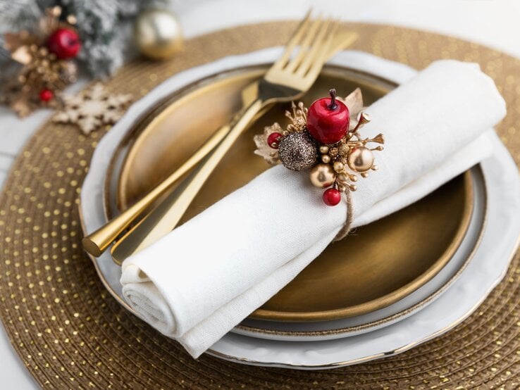 Weihnachtsdeko: Goldener Teller mit weißer Serviette und handgefertigtem Serviettenring aus glänzenden Kugeln und Beeren.