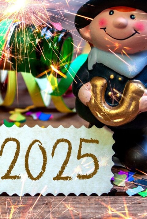 Glücksbringer-Figur mit goldenem Hufeisen, Kleeblatt, bunten Luftschlangen und Wunderkerzen vor einer Karte mit „2025“.