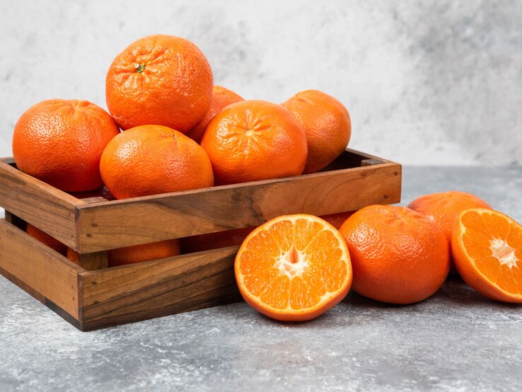 Obstkisten aus Holz mit Orangen gefüllt steht auf einem grauen Untergrund und auch der Hintergrund ist grau.