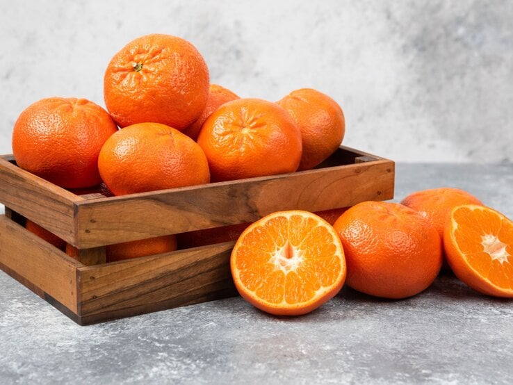 Obstkisten aus Holz mit Orangen gefüllt steht auf einem grauen Untergrund und auch der Hintergrund ist grau.