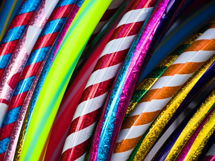 Bunte Hula-Hoop-Reifen mit glänzenden, spiralförmigen Mustern in Rot, Blau, Gelb und Neonfarben liegen dicht aneinander.