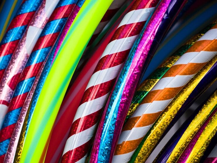 Bunte Hula-Hoop-Reifen mit glänzenden, spiralförmigen Mustern in Rot, Blau, Gelb und Neonfarben liegen dicht aneinander.