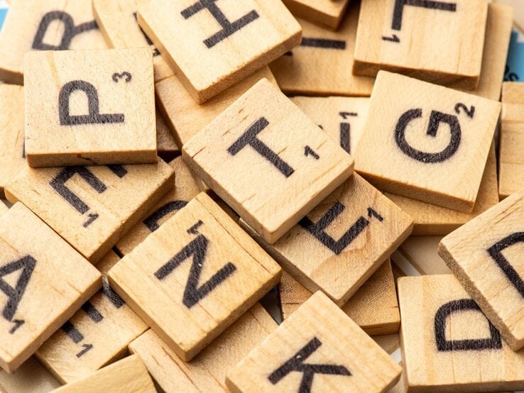 Ein Haufen hölzerner Scrabble-Buchstabensteine mit schwarzen Lettern liegt chaotisch durcheinander.