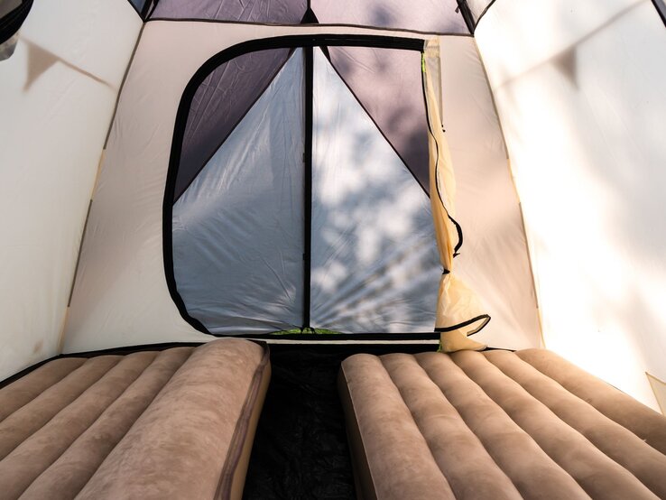 Zwei bequeme Luftmatratzen in einem lichtdurchfluteten Zelt mit geschlossenem, dreieckigem Eingang.
