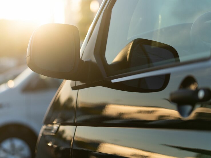Ein parkendes schwarzes Auto, dessen Seitenspiegel von der untergehenden Sonne angestrahlt wird, daneben ein weißes Fahrzeug.
