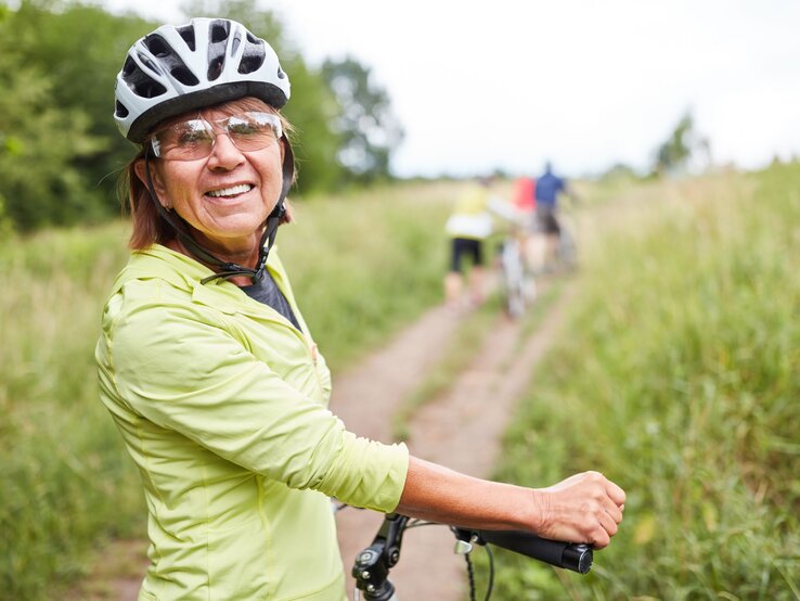 Ältere Frau auf dem Fahrrad trägt einen Fahrradhelm in der Natur.