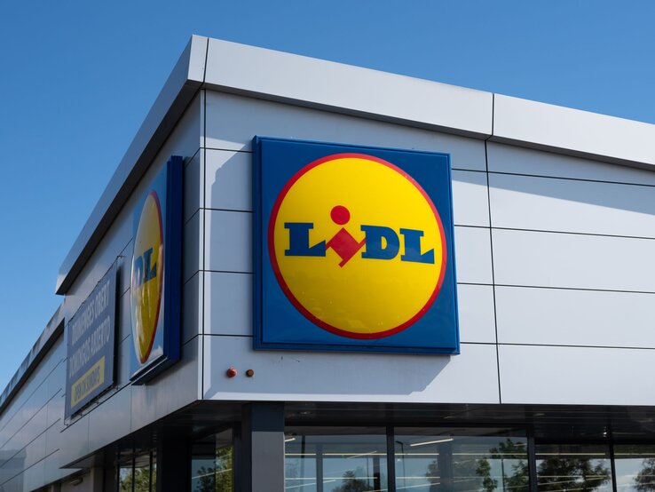 Außenansicht eines modernen Lidl-Supermarkts mit großem, leuchtendem Logo unter blauem Himmel.