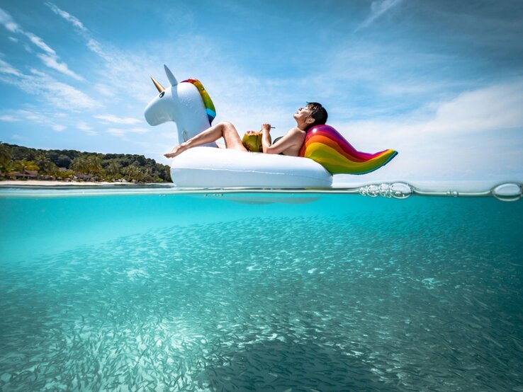 Eine Frau sitzt auf einem aufgeblasenen Einhorn aus Plastik und treibt damit in einem Pool. | © gettyimages/	Khaichuin Sim