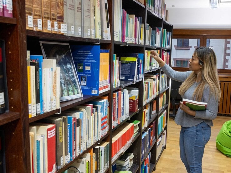 Eine Frau steht vor einem Bücherregal und hält Bücher in der Hand | © BILD der FRAU