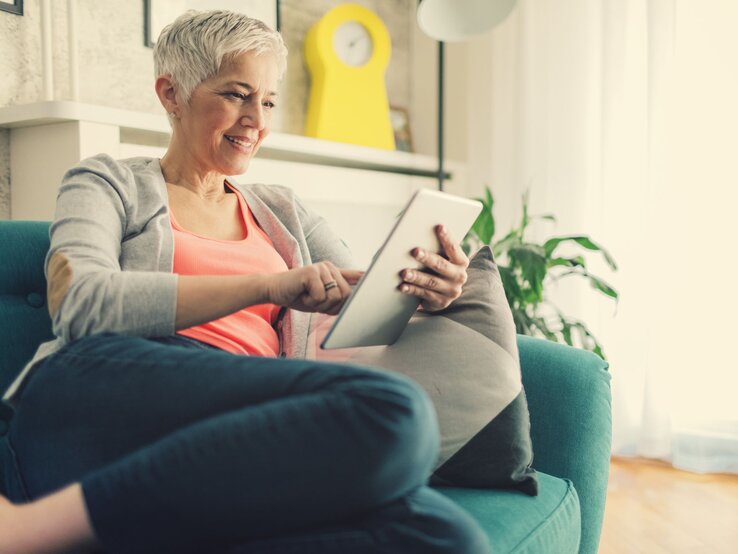 Frau guckt ein Tablet und sitzt auf dem Sofa.