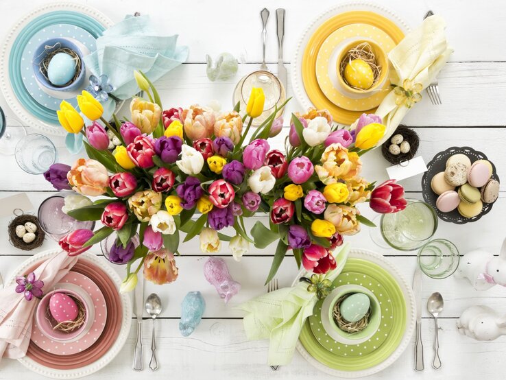 Bunte Tulpen in Gelb, Rot, Rosa und Lila schmücken eine festlich gedeckte Ostertafel mit pastellfarbenem Geschirr und verzierten Ostereiern.