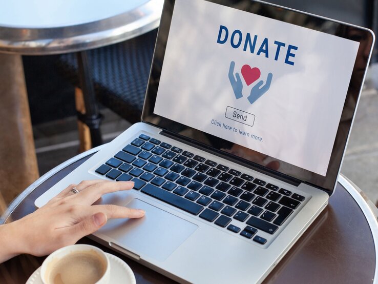 Zu sehen ist eine Laptop auf dem Donate steht und Frauenhände, die diesen bedienen.