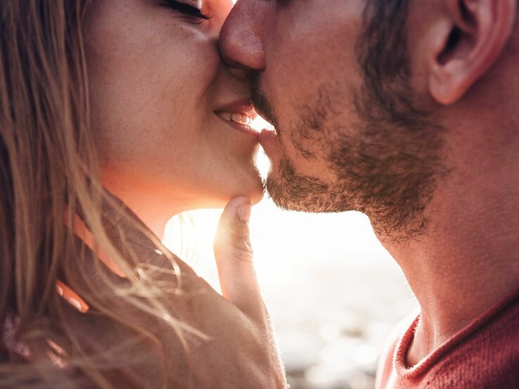 Mann und Frau küssen sich. Beide scheinen sich in einem romantischen Moment zu befinden, wobei der Mann sanft das Kinn der Frau berührt und sie sich gegenseitig sehr nahe sind.