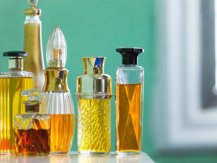Verschiedene elegante Parfümflaschen mit goldgelbem Inhalt auf einer Oberfläche, vor einem unscharfen grünen Hintergrund.
