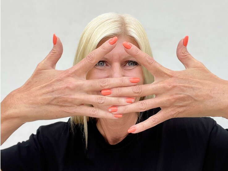 Topage-Model Renate Zott mit pfirsichfarbenen Fingernägeln – ihre Hände hält sie gekreuzt vor dem Gesicht.