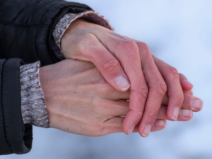 Hände, die ineinander gelegt sind, vermutlich um sich zu wärmen. Die Haut der Hände wirkt trocken und leicht gerötet, was auf kaltes Wetter oder trockene Winterluft hindeutet.