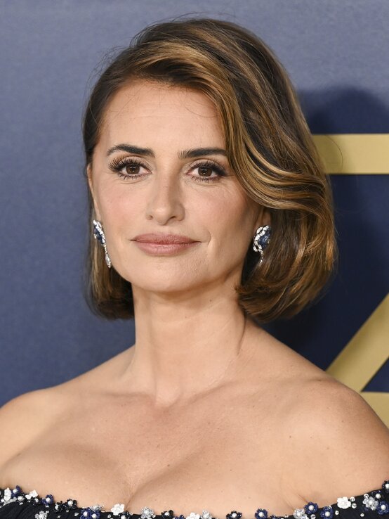 Penelope Cruz mit schulterlangem, welligem braunen Haar, die ein elegantes, schulterfreies Kleid trägt.  | © Getty Images / Gilbert Flores 