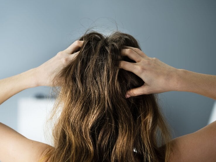 Frau von hinten mit verwuscheltem braunem Haar fasst sich mit den Händen in die Haare.