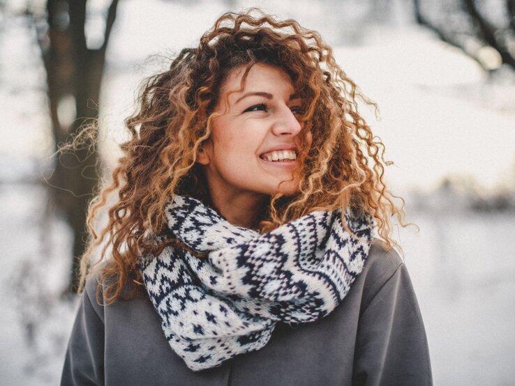 Zu sehen ist eine Frau mittleren Alters, die ihre Locken im Winter offen trägt