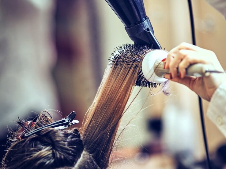 Zu sehen sind Haare, die mithilfe einer Rundbürste in ein Blowout geföhnt werden.