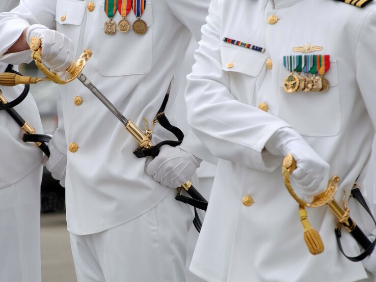 Gruppe von Männern in weißen Militäruniformen, die goldene Schwerter halten. Die Uniformen haben eine Reihe von Auszeichnungen und Medaillen auf der Brust und sind mit goldenen Knöpfen versehen. | © Getty Images / pixhook