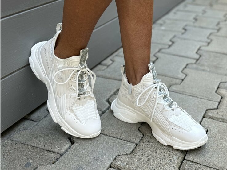 Beine, die in weißen Sneakers stecken. Die Schuhe haben eine dicke Sohle und sind mit weißen Schnürsenkeln versehen. Sie scheinen aus einem Mix aus Leder und atmungsaktivem Stoff zu bestehen, was ihnen einen sportlichen und modernen Look verleiht. | © Renate Zott