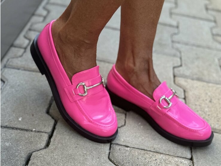 Beine, die in leuchtend pinken Loafern stecken. Diese Schuhe haben eine glänzende Oberfläche und sind mit einer silbernen Schnalle dekoriert.  | © Renate Zott