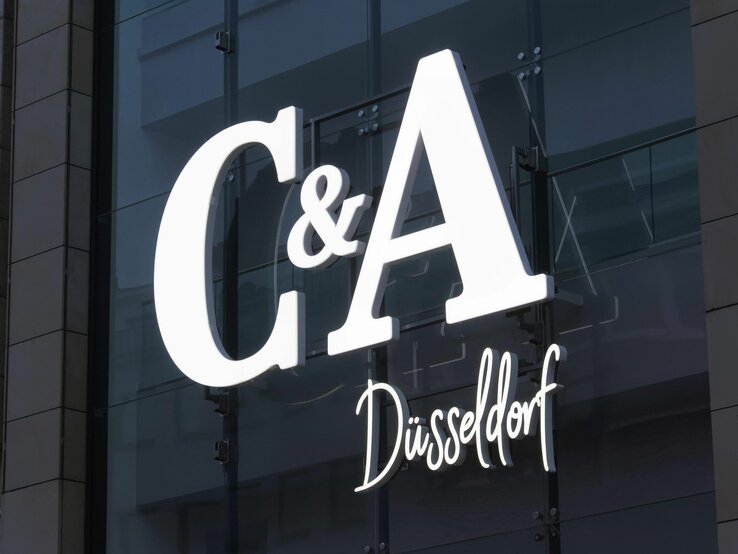 Leuchtendes C&A-Logo mit Schriftzug "Düsseldorf" an einer Glasfassade mit Spiegeleffekt.