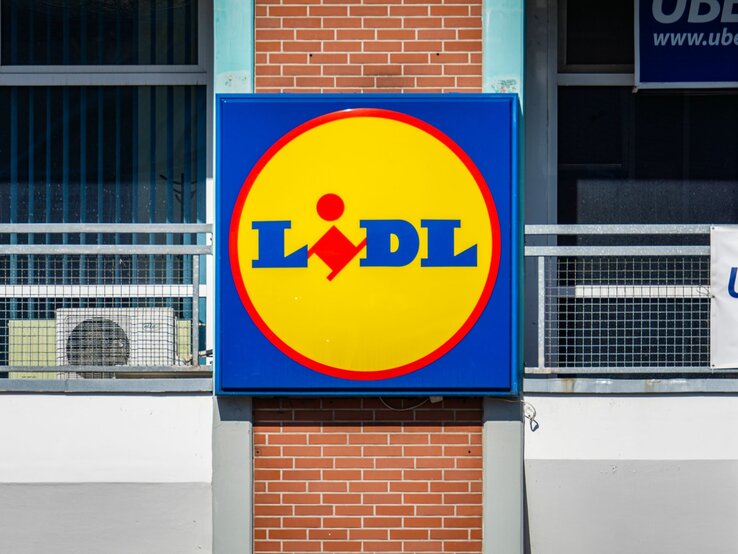 Großes Lidl-Logo in Gelb und Blau an der Außenwand eines Gebäudes mit roten Ziegeln.