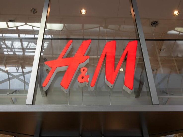 Großes H&M-Logo in leuchtendem Rot an einer gläsernen Fassade, reflektiert das Innenlicht.