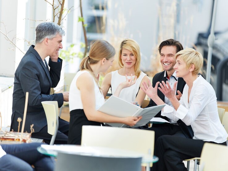 Geschäftsleute, die bei einem informellen Meeting im Freien sitzen. Die Personen sind in Business-Kleidung gekleidet und scheinen in einer lebhaften Diskussion engagiert zu sein.