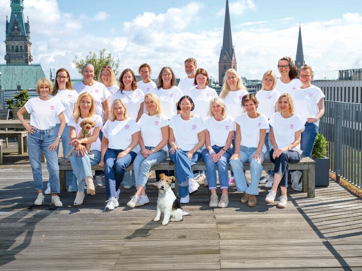 Das BILD der FRAU Team in weißen T-Shirts und Jeans posiert auf einer Dachterrasse vor dem Hamburger Rathaus, zwei Hunde sitzen dabei.