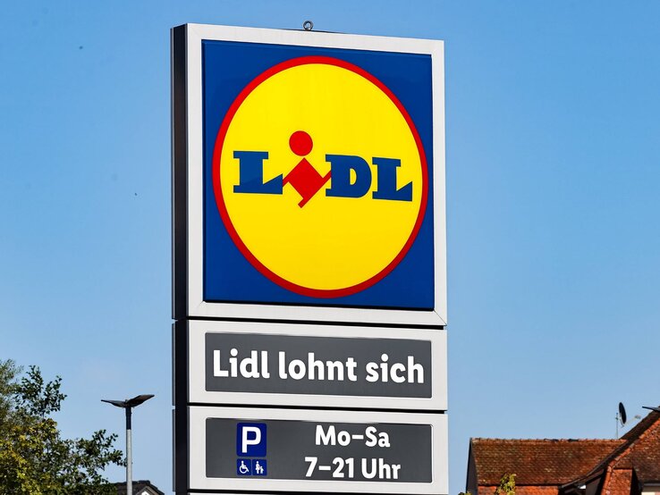 Ein Schild mit dem Lidl-Logo und dem Slogan "Lidl lohnt sich" vor klarem, blauem Himmel und Gebäuden im Hintergrund.