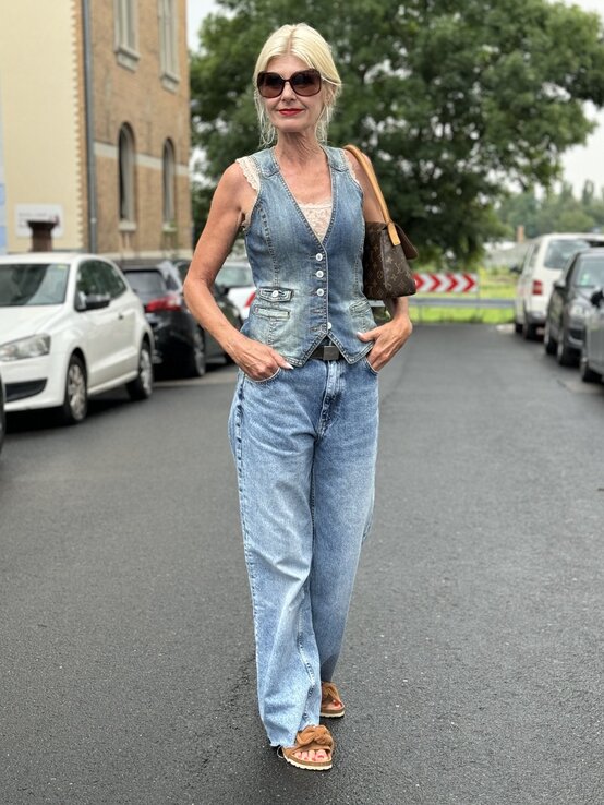  Frau in sommerlichem Outfit mit blonden Haaren und Sonnenbrille. Ihr Outfit besteht aus einer Jeansweste über einem Spitzen-Top, kombiniert mit einer weit geschnittenen Jeanshose. | © Renate Zott