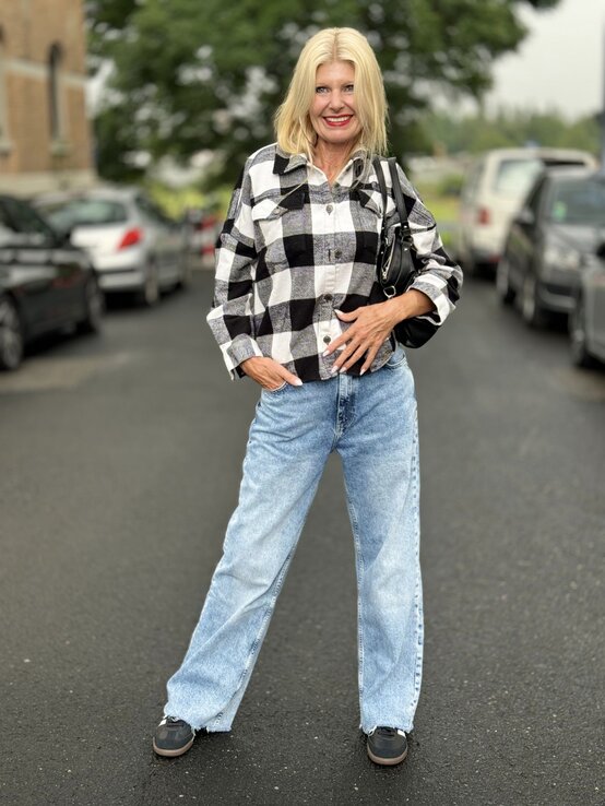 Frau mit blonden Haaren, die in einem lässigen, karierten Hemd in Schwarz-Weiß und einer hellen Jeans gekleidet ist.  | © Renate Zott