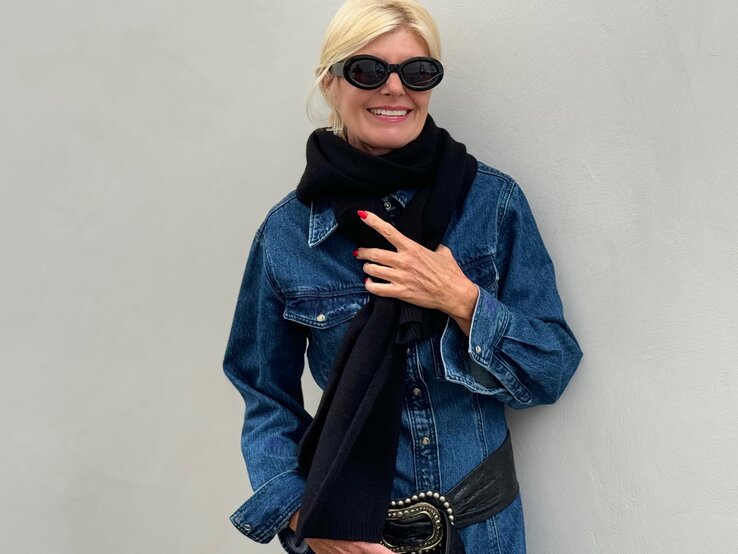 Stilvolle Frau in einem lässigen Herbst-Outfit. Sie trägt eine dunkle Sonnenbrille, einen schwarzen Schal und eine dunkelblaue Jeansjacke.