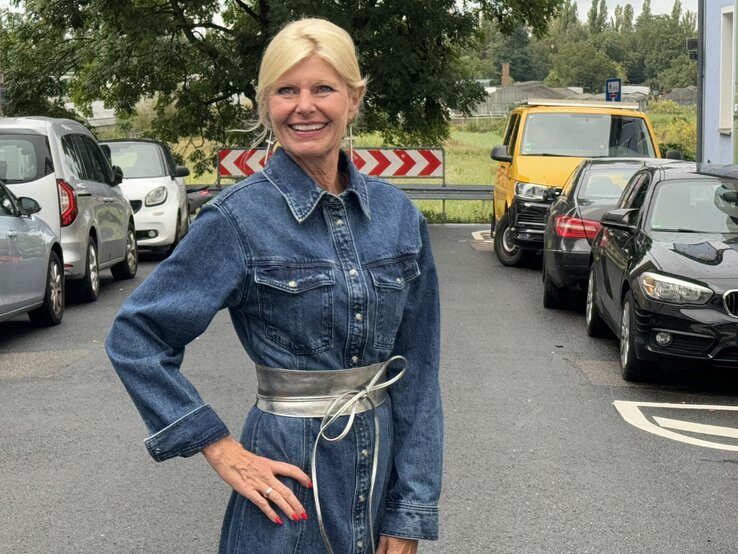 Frau trägt ein Jeanskleid mit langen Ärmeln und hat einen breiten, silberfarbenen Taillengürtel umgebunden | © Renate Zott