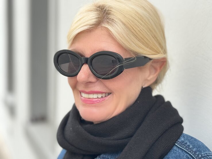 Nahaufnahme einer Frau, die eine auffällige, ovale Sonnenbrille trägt. Die Sonnenbrille hat breite, schwarze Rahmen und verleiht ihrem Look eine moderne, stilbewusste Note. | © Renate Zott