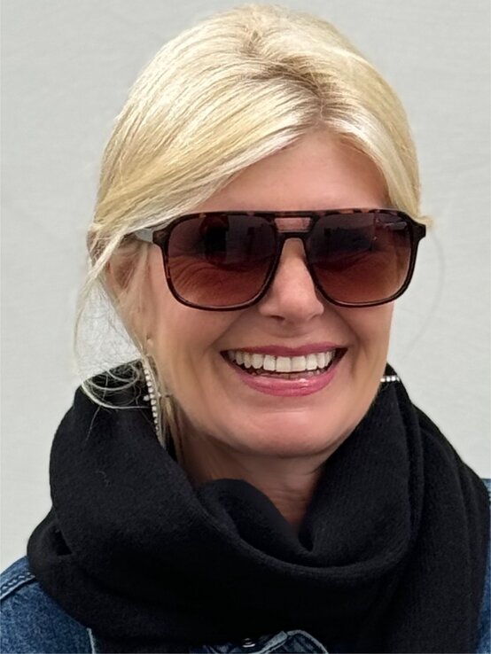  Nahaufnahme einer Frau mit blonden Haaren, die eine markante Retro-Sonnenbrille trägt. Die Brille hat einen dunklen Rahmen in Schildpatt-Optik und großflächige Gläser, die das Gesicht stilvoll umrahmen. | © Renate Zott