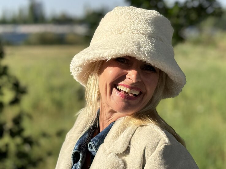 Lächelnde Frau, die einen cremefarbenen Bucket Hat aus flauschigem Material trägt. Der Hut verleiht ihrem Look einen gemütlichen, winterlichen Touch. | © Renate Zott