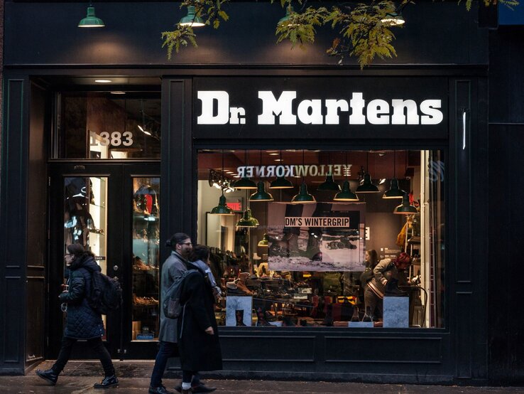 Außenansicht eines Dr. Martens Stores bei Abenddämmerung, Passanten gehen vor den beleuchteten Schaufenstern vorbei.