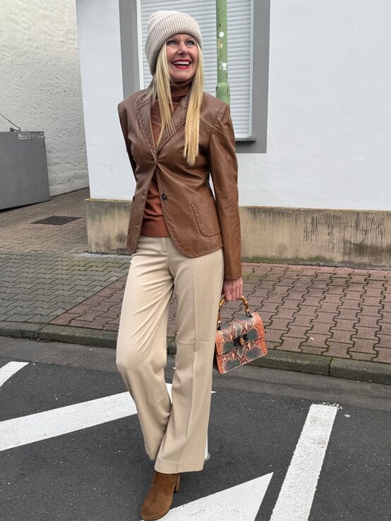 Elegant gekleidete Renate Zott in brauner Jacke, beiger Hose und Stiefeletten hält eine kleine Tasche mit Schlangenprint. | © Renate Zott