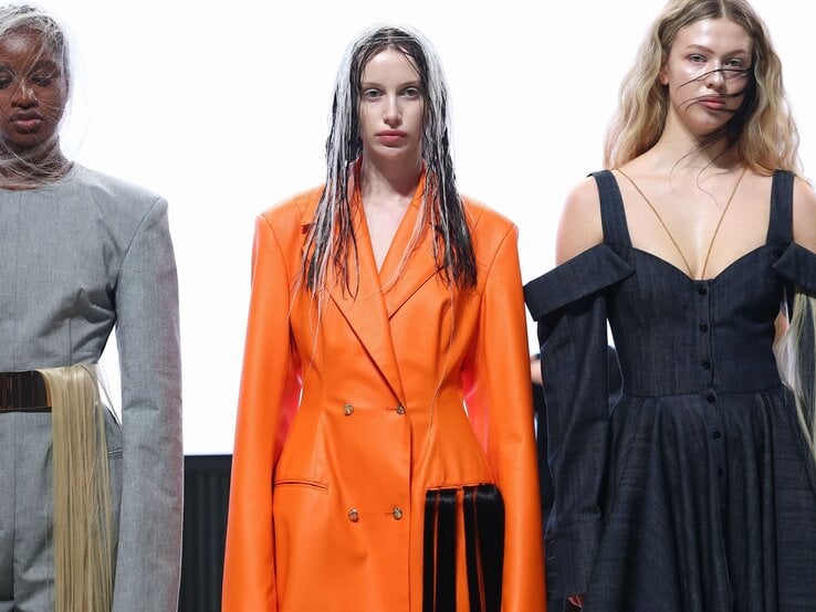 Frontale Aufnahme dreier Models mit futuristischen Looks, nassen Strähnen und kunstvollen Kleidern in Grau, Orange und Dunkelblau. | © Sebastian Reuter/Getty Images for Rebekka Ruetz