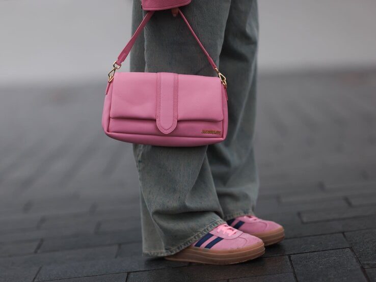 Detailaufnahme einer rosa Handtasche mit goldener Schnalle, getragen zu lässiger Jeans und farblich abgestimmten Sneakers.