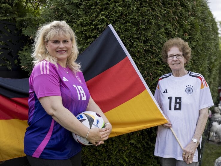 Viola Mittelstädt steht vor einer Deutschlandflagge, die Oma Angelika hält. Beide tragen ein Deutschlandtrikot und Viola hält einen Fußball in der Hand.