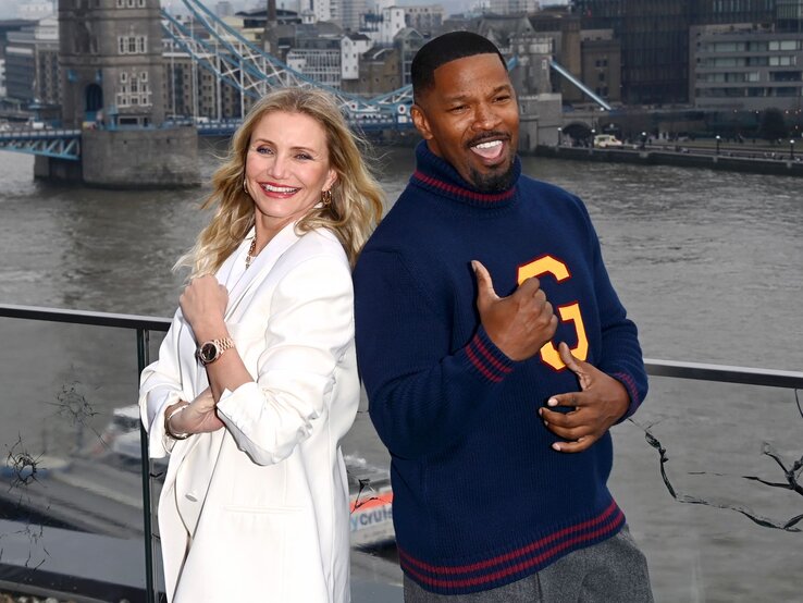 Cameron Diaz im weißen Blazer und Jamie Foxx in blauem Pullover mit gelbem „G“ posieren lächelnd vor der Tower Bridge in London. | © Stuart C. Wilson/Getty Images