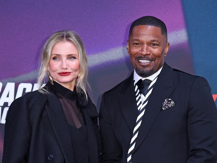 Cameron Diaz mit blonden Haaren, rotem Lippenstift und Jamie Foxx im dunklen Anzug stehen nebeneinander und lächeln vor einer bunten Wand.