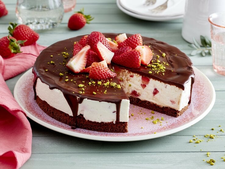 Joghurt-Erdbeer-Torte auf einem rosa Teller auf hellgrünem Hintergrund. Rechts Geschirr und links rosa Geschirrtuch. 